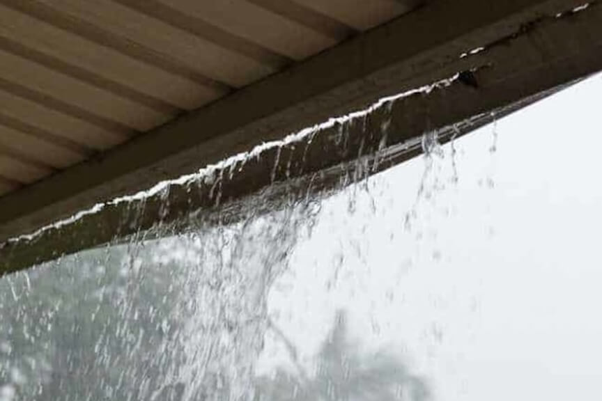 Water dripping from a seam or crack in a gutter, indicating a leak