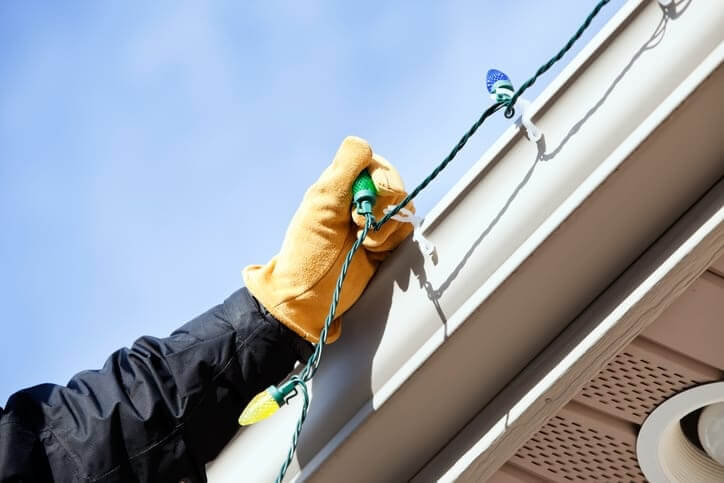 A person on a ladder carefully clipping Christmas lights to a gutter