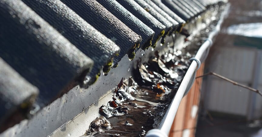 An overflowing gutter with water pouring over the sides during a rainstorm