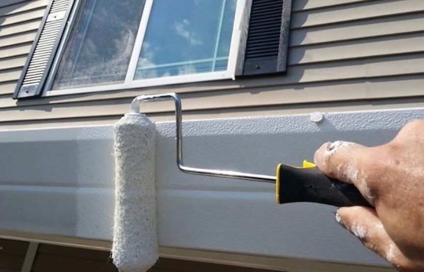 A person using a paintbrush to apply paint to a section of a gutter