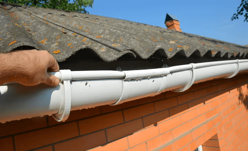 A close-up of a leaky gutter with water dripping from a seam