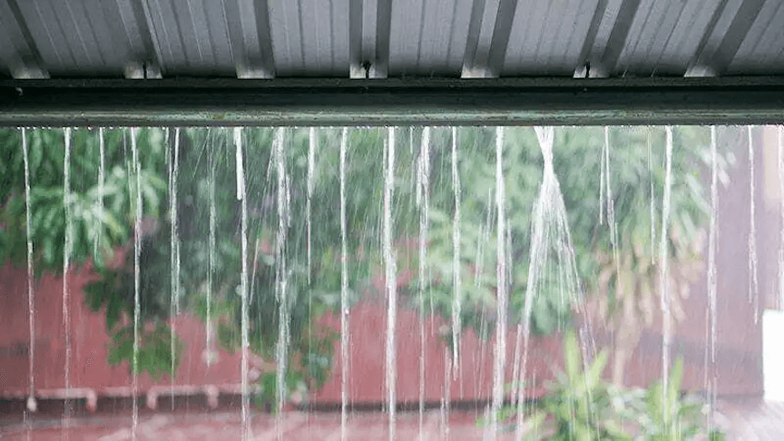 A dramatic image of a house with water pouring off the roof and pooling around the foundation